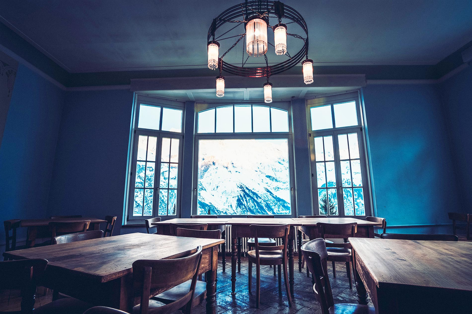 Una grande finestra con vista sulle Alpi innevate rischiara un’ampia sala da pranzo con tavoli e sedie in legno massiccio.