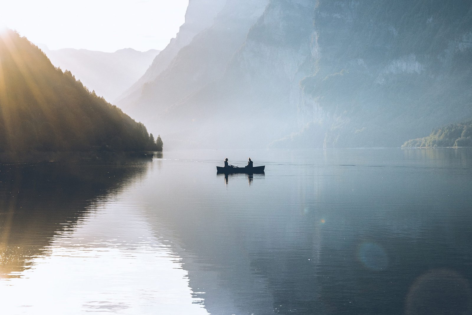 Zwei Personen sitzen in einem kleinen Ruderboot inmitten eines Sees. Die Abendsonne verschwindet langsam hinter den nahen Bergen.