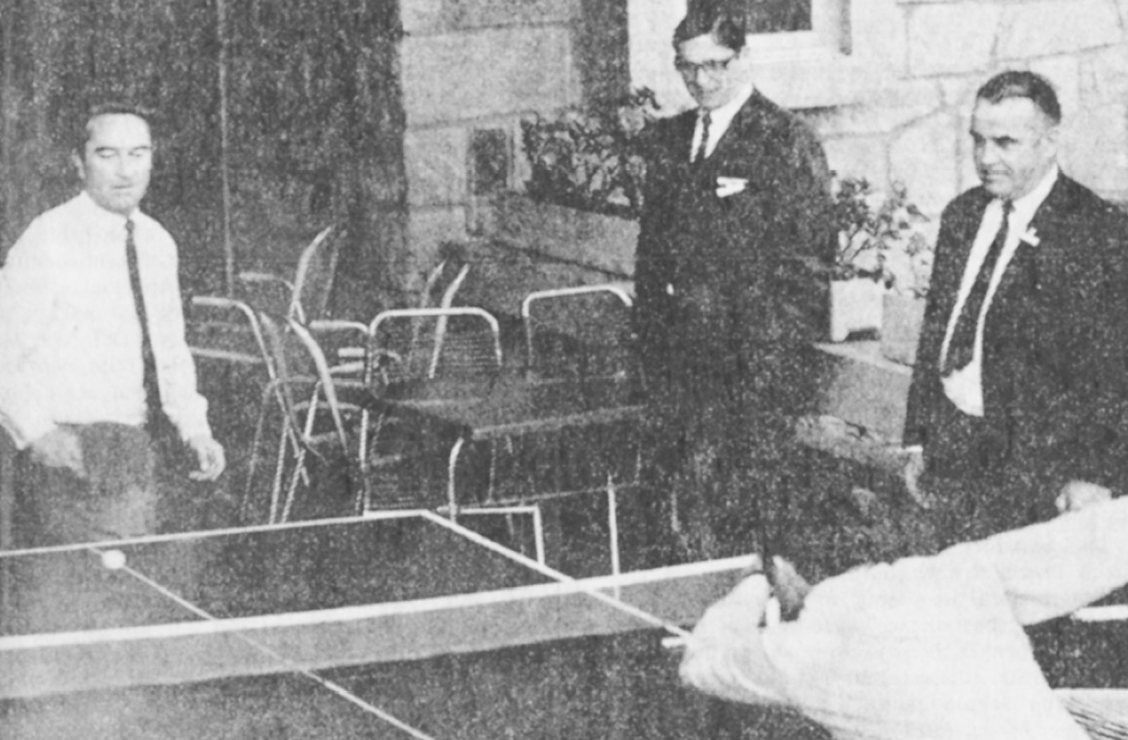 Vier Männer stehen auf einer Terrasse um eine Pingpongplatte. Während zwei spielen, schauen die anderen zu.
